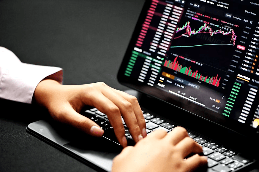 Trader working on a laptop while monitoring financial markets and investment positions.